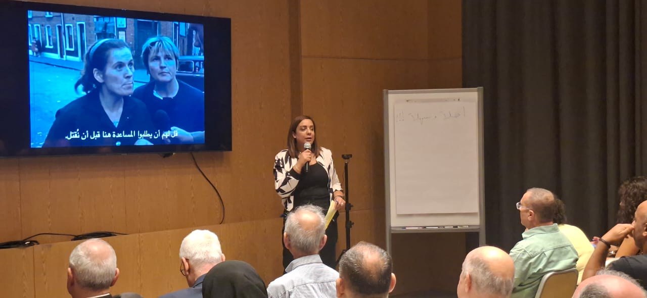 Roweida Saleh speaking to the audience in front of a screen showing the film